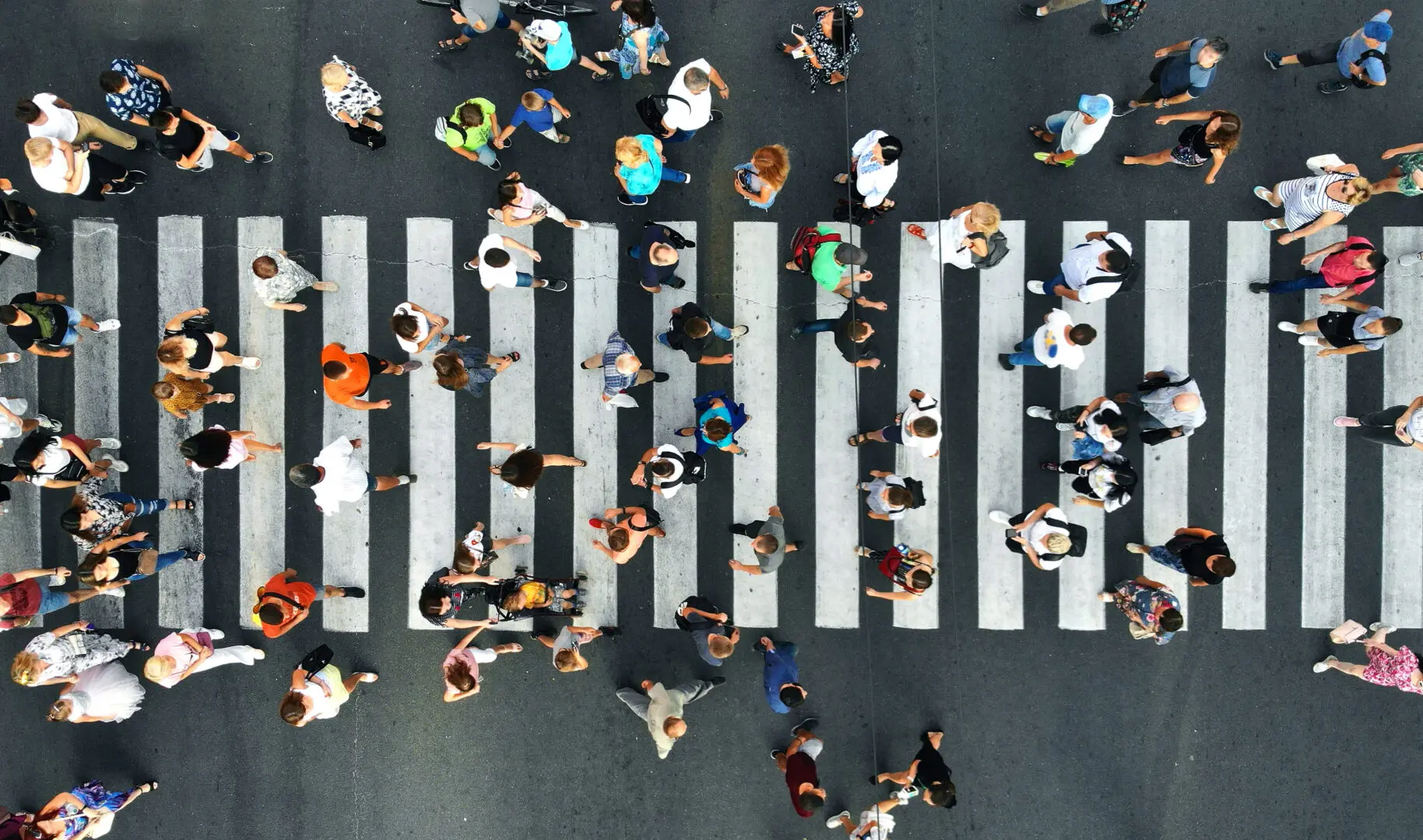 Aerial view of a busy pedestrian crosswalk with people walking in various directions on a sunny day.