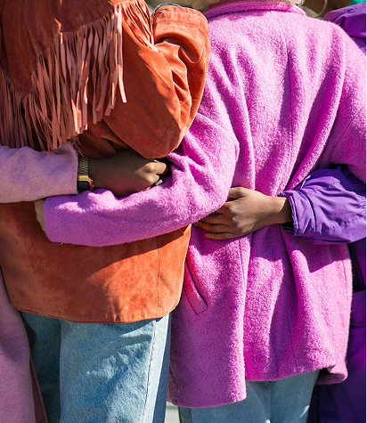 Four people dressed in colorful jackets stand closely together with their arms around each other's backs.