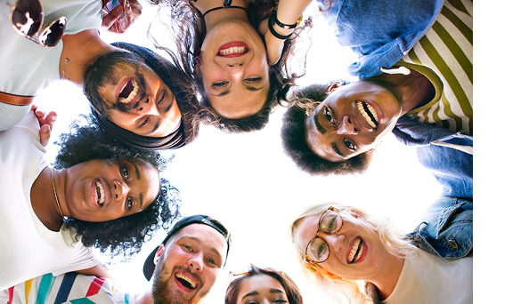 A group of seven people stand in a circle outdoors, looking down at the camera and smiling.