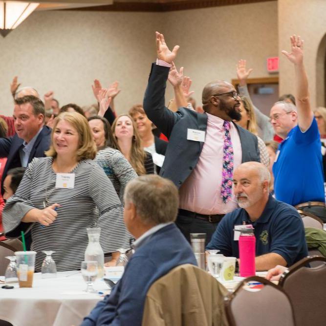 A group of people raising their hands at a conference.