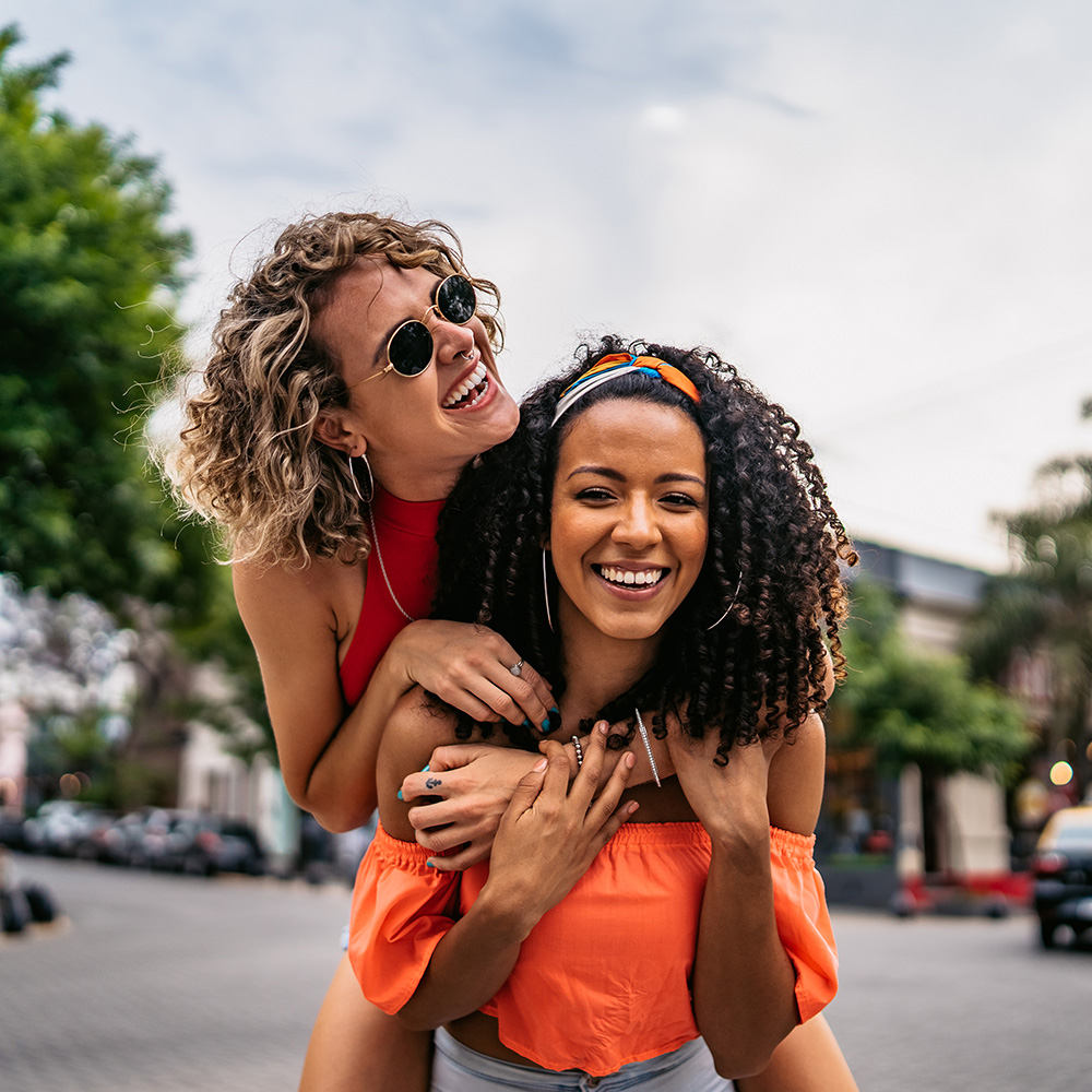 Two women smiling while riding on each other's shoulders.