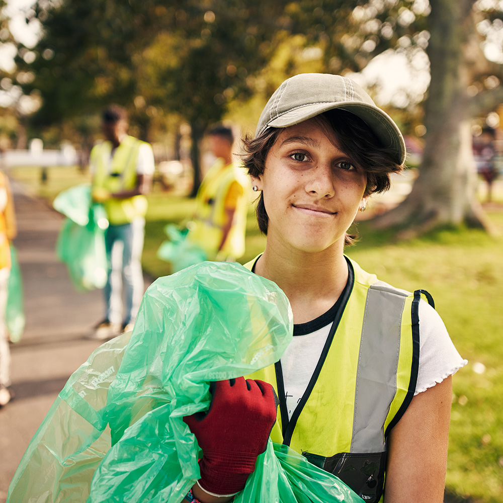 A girl in a green vest holding a garbage bag.