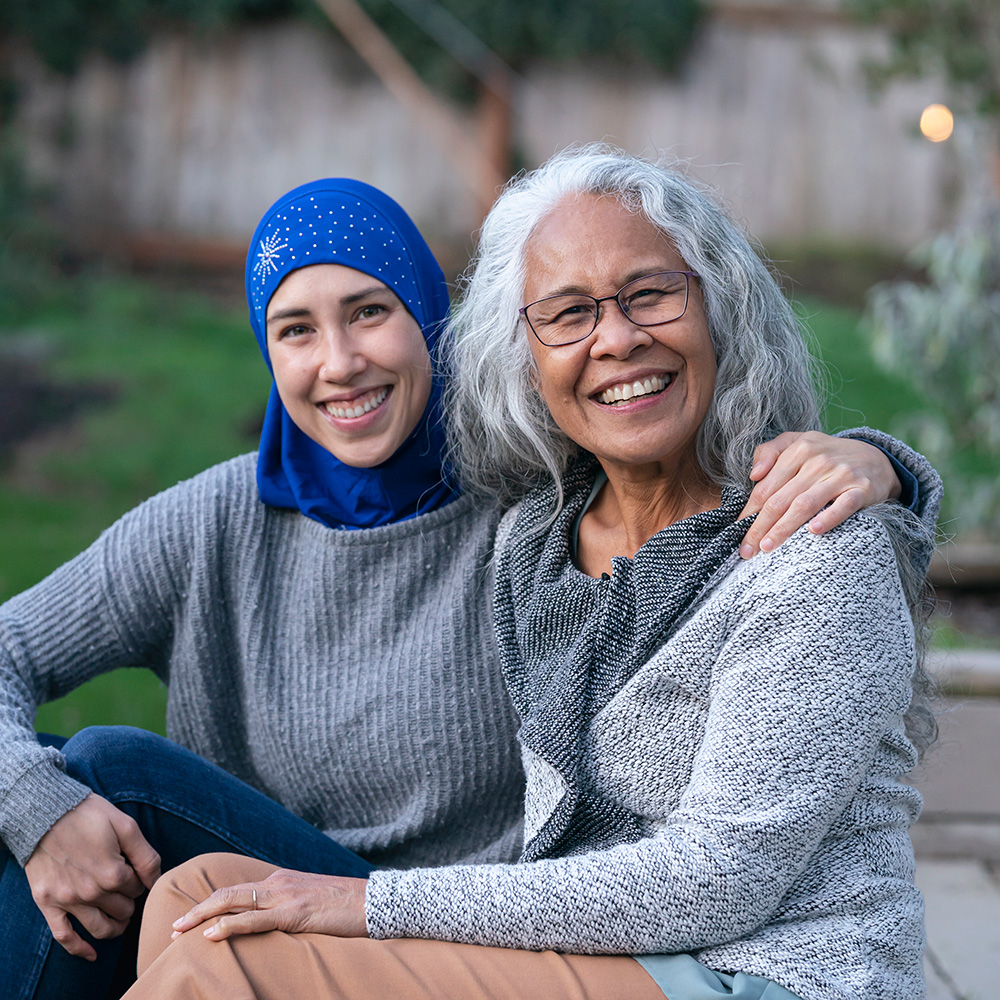 A woman in a hijab smiles with an older woman.
