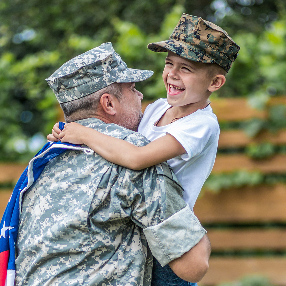 A soldier is hugging a young boy with an american flag.