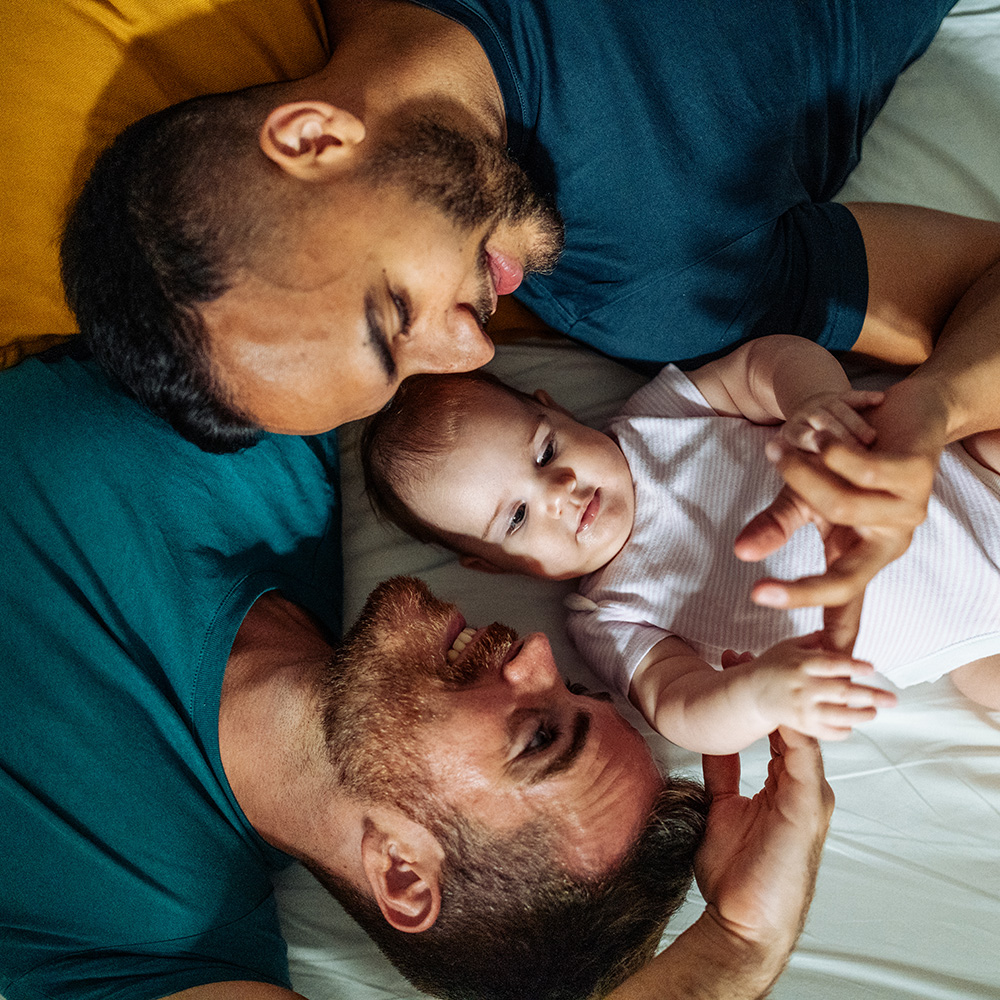 Three men and a baby laying on a bed.