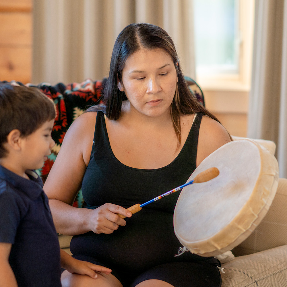 A pregnant woman playing a drum with a young boy.