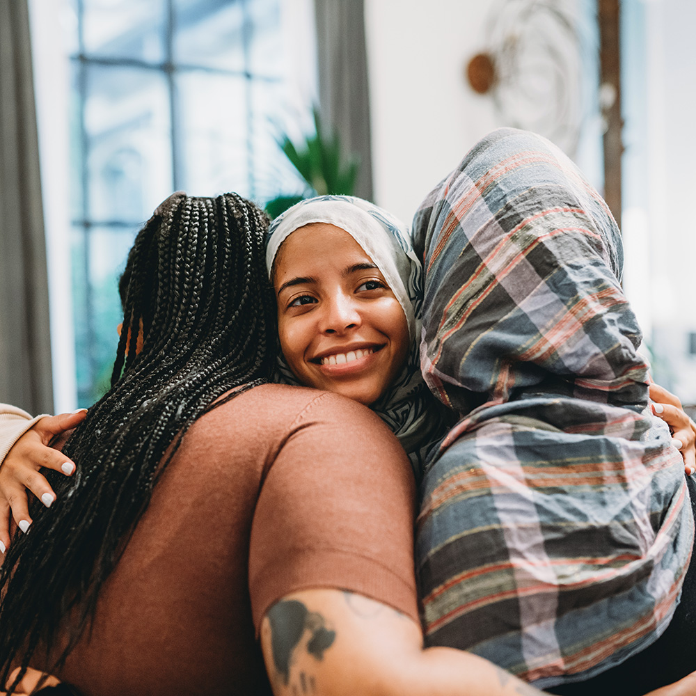 Three muslim women hugging each other in a living room.