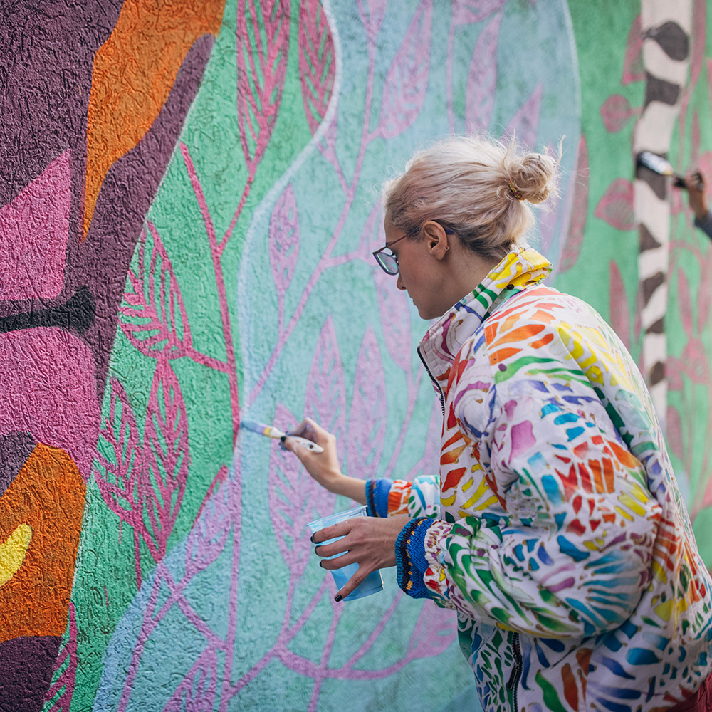 A woman is painting a mural on a wall.