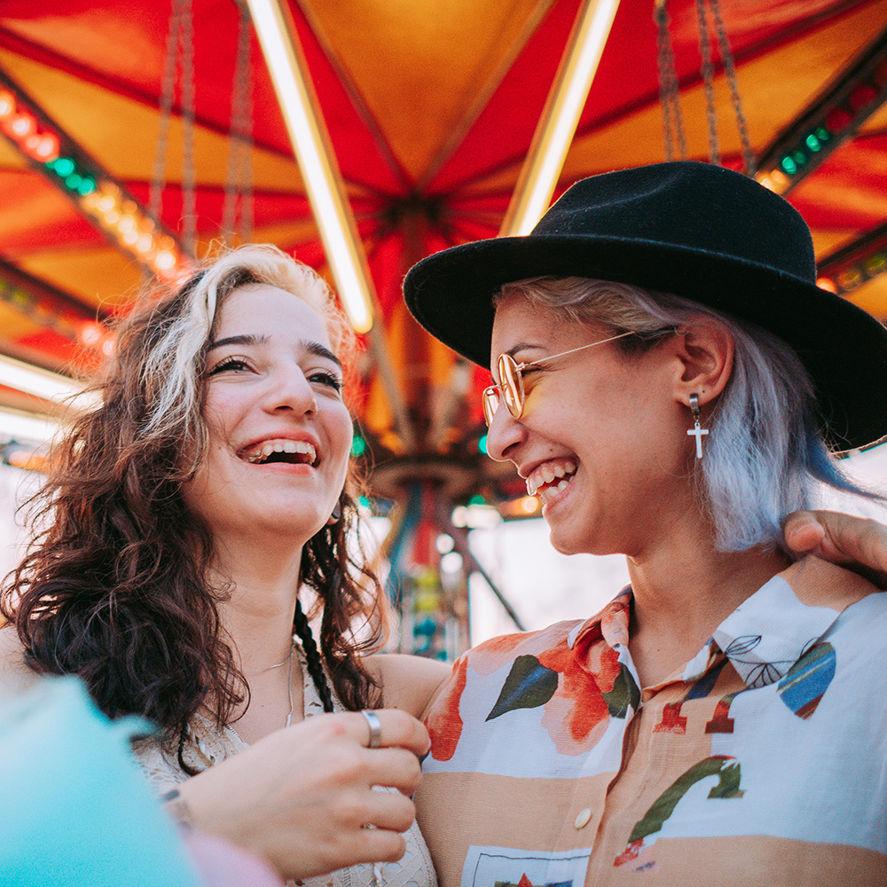 Two women smiling at each other at a carnival.