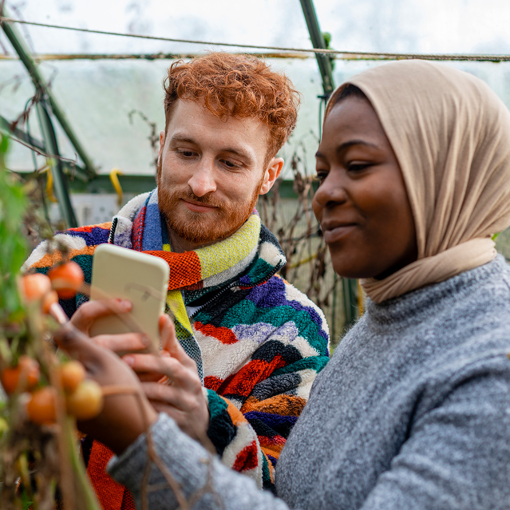 Two people looking at a cell phone in a greenhouse.