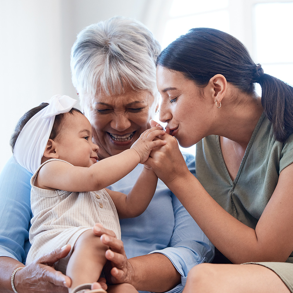 A woman is holding a baby and an older woman is touching her finger.