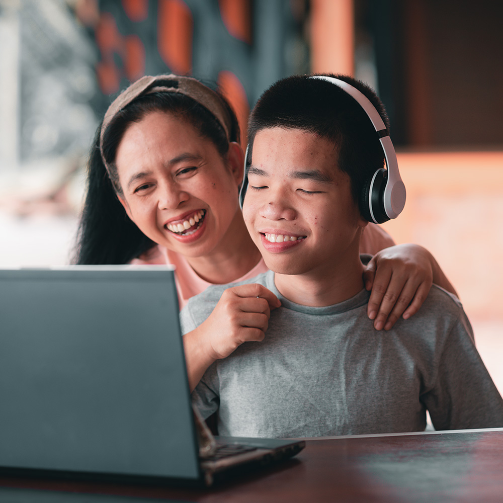 A mother and son are smiling while using a laptop.