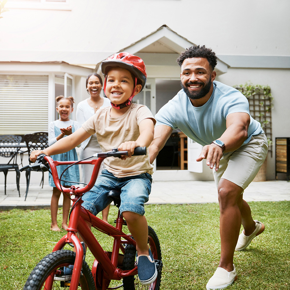 A man and his son riding a bike in the backyard.