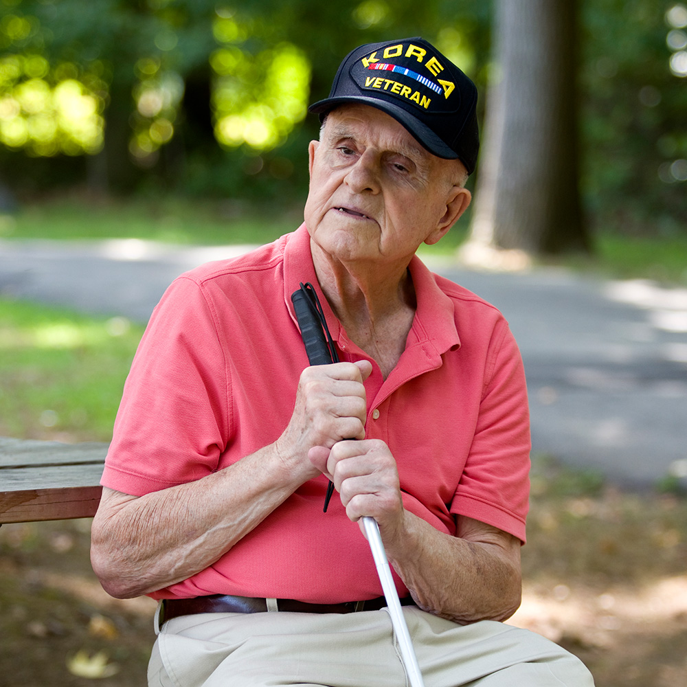An older man sitting on a bench holding a cane.