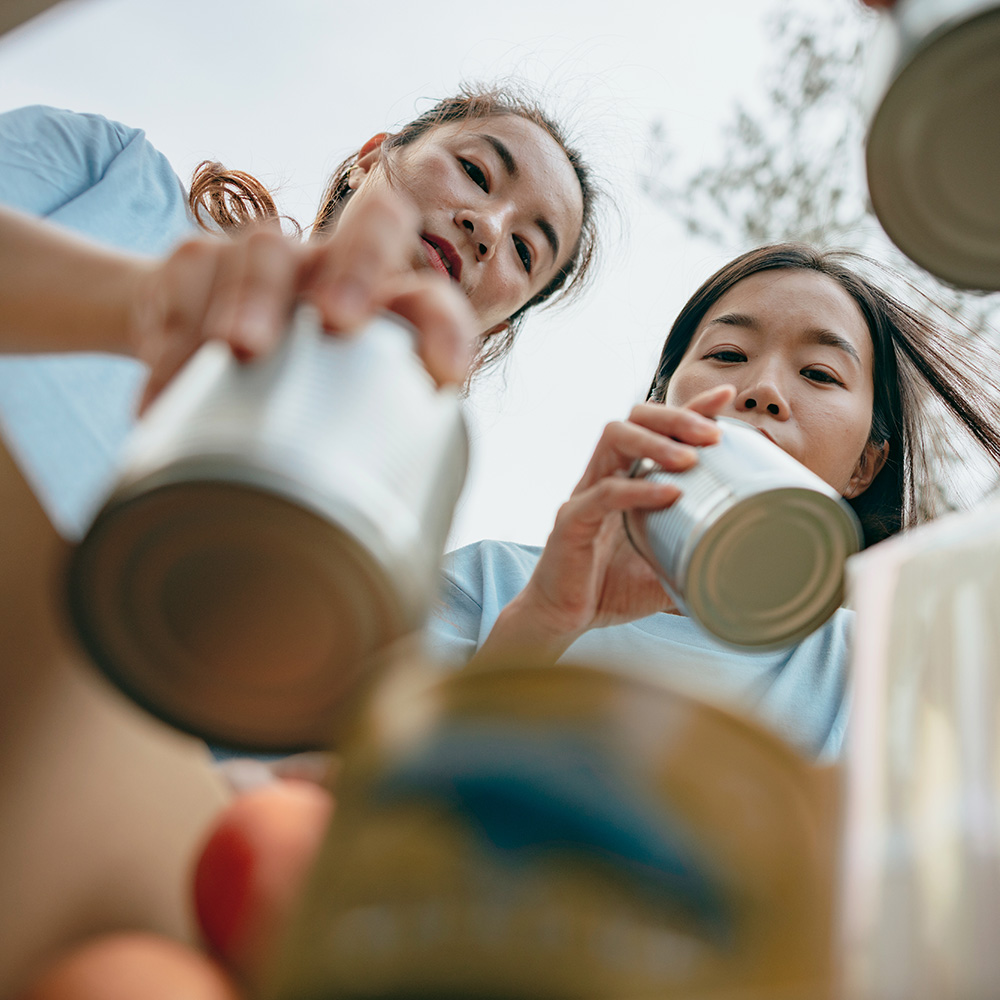 Two asian women are holding cans of food.