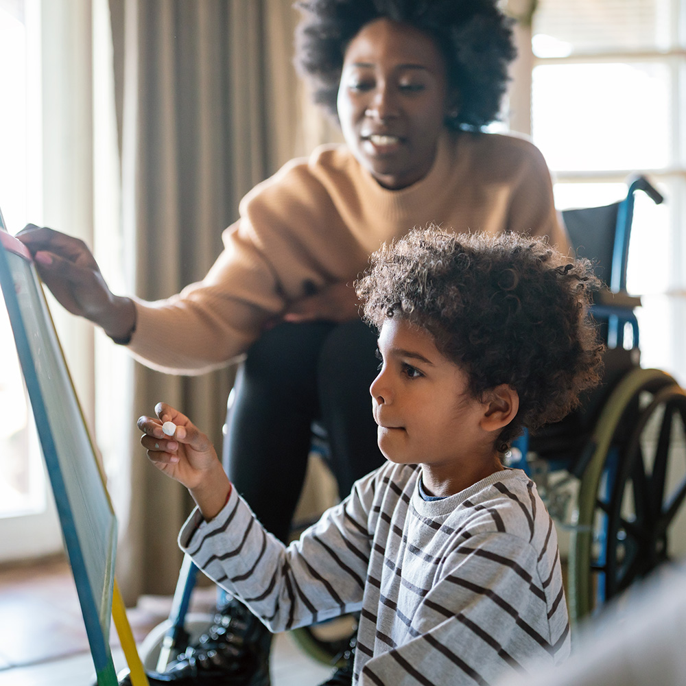 A woman in a wheelchair with a child drawing on a easel.