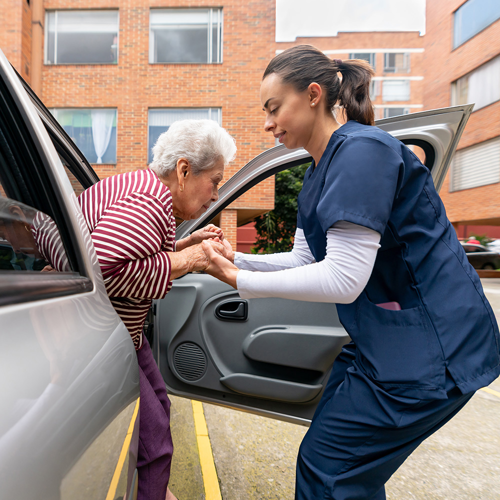 A nurse helping an elderly woman out of a car.