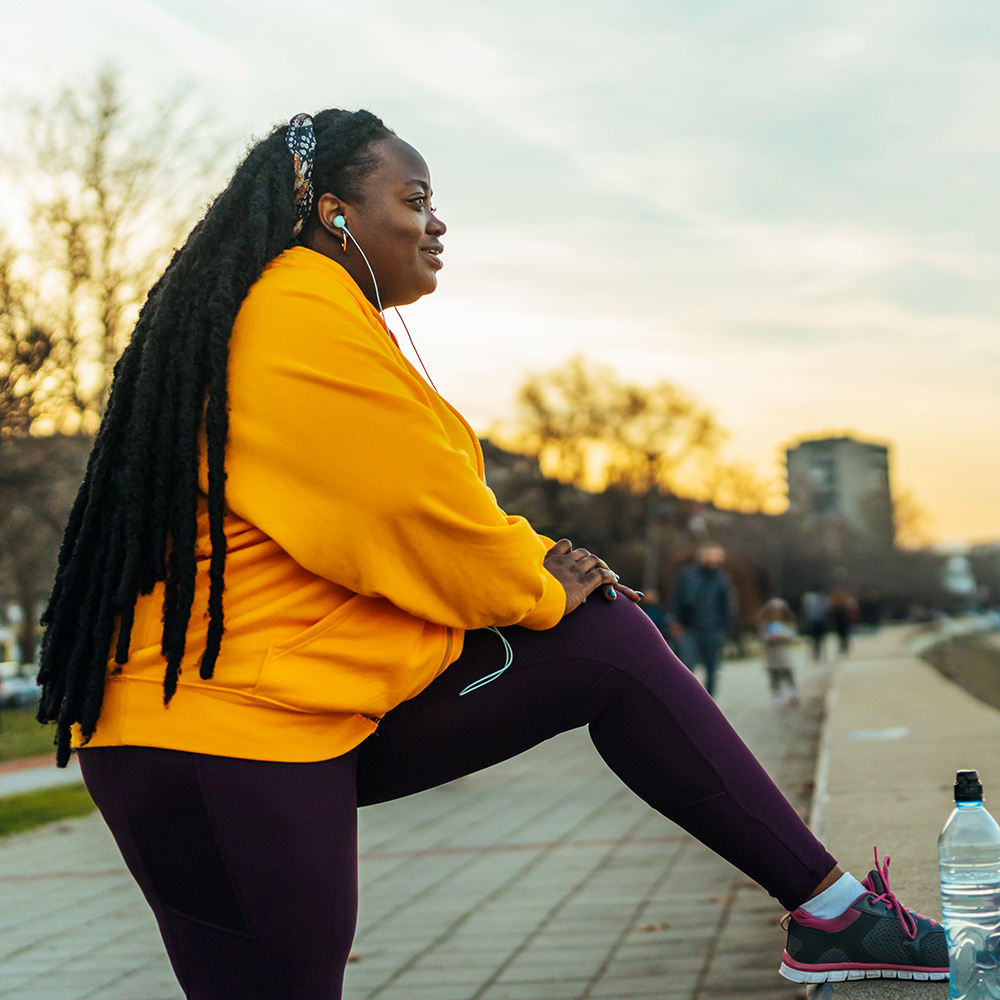 A woman with dreadlocks sitting on a bench listening to music.