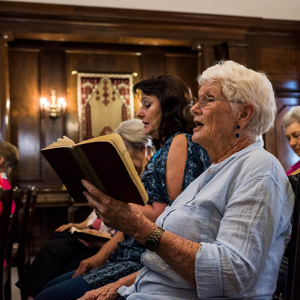 A group of older women are sitting in a room and reading a book.