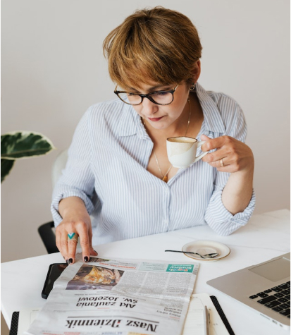 A woman sitting at a desk with a cup of coffee and a newspaper.